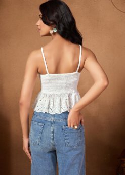 White sleeveless smocked crop top with intricate eyelet lace detailing paired with blue jeans